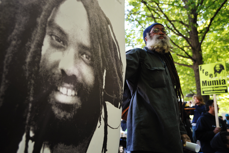 A protestor stands next to an image of Mumia Abu-Jamal outside the US Department of Justice on April 24, 2012 in Washington, DC, calling for the release from prison of the ex-Black Panther militant, who was convicted for the killing of a white police officer in 1981 and sentenced to death. In December 2011 prosecutors gave up their effort to execute Abu-Jamal, who supporters believe is innocent and was framed for the murder in the racially charged case. Supporters decided to hold their demonstration on April 24, 2012, Abu-Jamal's 58th birthday. AFP PHOTO / Mandel NGAN (Photo credit should read MANDEL NGAN/AFP/Getty Images)